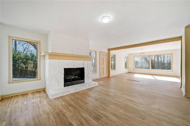 unfurnished living room featuring baseboards, visible vents, a fireplace with raised hearth, and wood finished floors