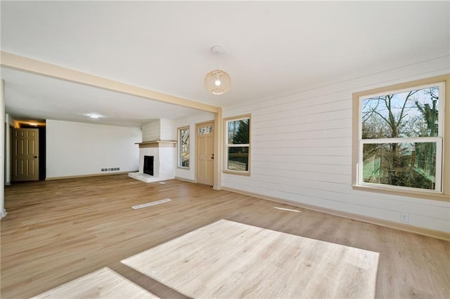 unfurnished living room with light wood-style floors, baseboards, a fireplace, and visible vents