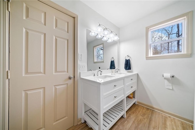 full bath featuring double vanity, a sink, baseboards, and wood finished floors