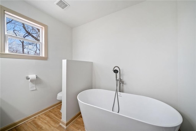 full bathroom featuring visible vents, a freestanding bath, toilet, wood finished floors, and baseboards