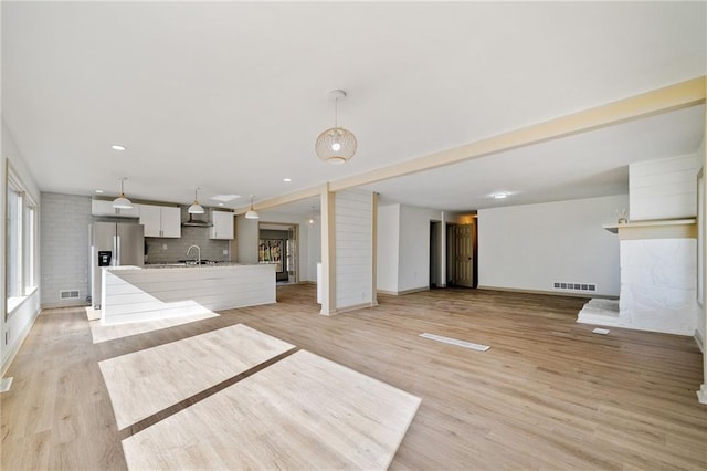 unfurnished living room with visible vents, a sink, and light wood-style flooring