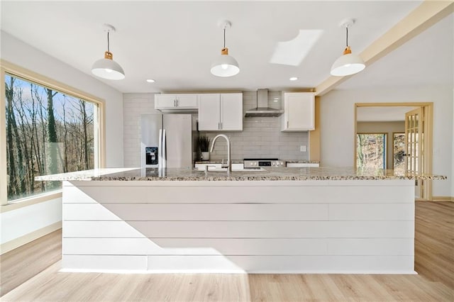 kitchen with light wood-style flooring, a sink, wall chimney range hood, stainless steel refrigerator with ice dispenser, and decorative backsplash