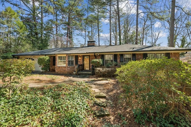 ranch-style house featuring brick siding, an attached garage, and a chimney