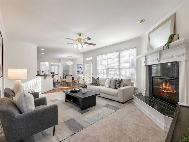 living room featuring a tile fireplace, ceiling fan, crown molding, and light colored carpet