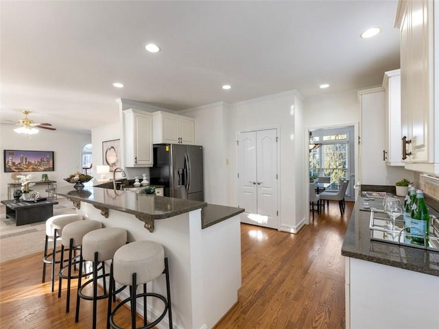 kitchen featuring kitchen peninsula, stainless steel refrigerator with ice dispenser, a breakfast bar, dark stone countertops, and white cabinetry