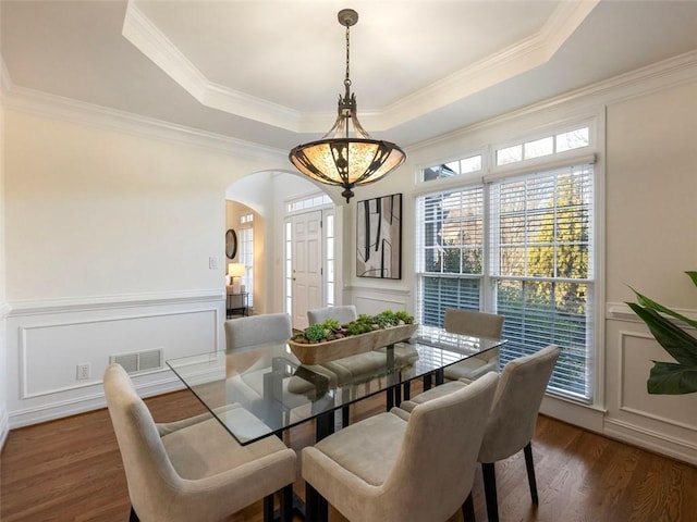 dining space with dark hardwood / wood-style floors, a raised ceiling, ornamental molding, and a chandelier