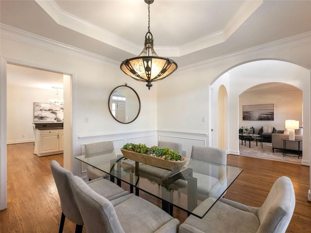 dining space featuring a raised ceiling, crown molding, a notable chandelier, and light wood-type flooring