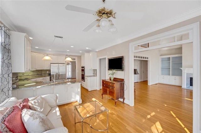 living area with a fireplace with flush hearth, ornamental molding, a ceiling fan, light wood-style floors, and baseboards