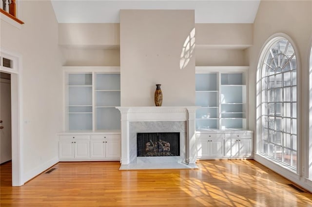 unfurnished living room with a fireplace, wood finished floors, visible vents, and baseboards