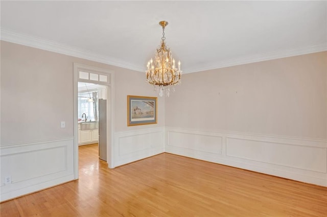 unfurnished room featuring light wood-style flooring, ornamental molding, a wainscoted wall, and a chandelier