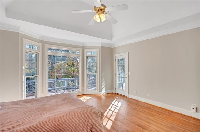 unfurnished bedroom with a tray ceiling, wood finished floors, access to exterior, and baseboards