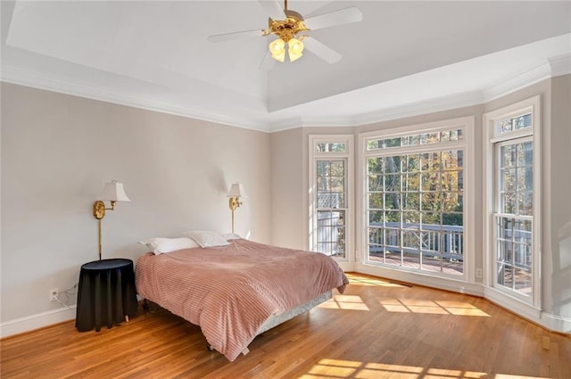 bedroom with wood finished floors, baseboards, access to exterior, crown molding, and a raised ceiling