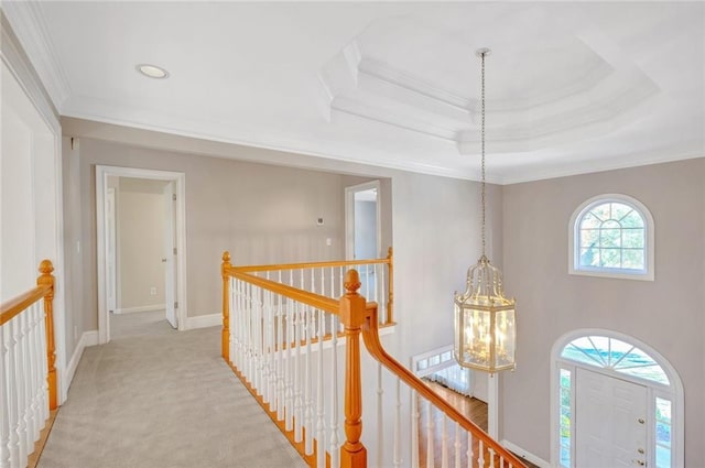 corridor featuring a tray ceiling, an upstairs landing, light colored carpet, and ornamental molding