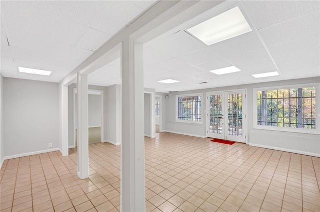 interior space featuring a drop ceiling, baseboards, a healthy amount of sunlight, and light tile patterned flooring