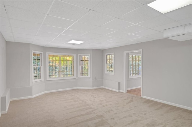 spare room with a drop ceiling, light carpet, and baseboards