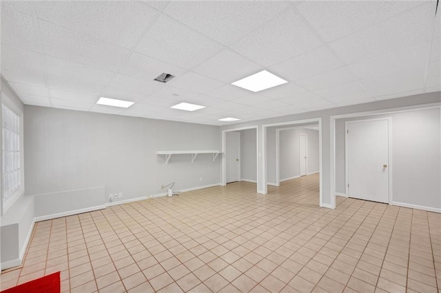 basement featuring light tile patterned floors, baseboards, and a paneled ceiling