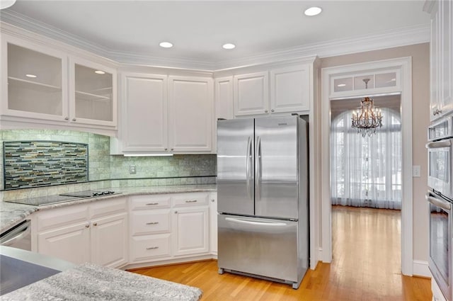 kitchen with light wood finished floors, glass insert cabinets, appliances with stainless steel finishes, a notable chandelier, and white cabinets