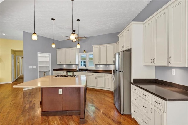 kitchen with stainless steel appliances, a textured ceiling, wood finished floors, a kitchen island, and white cabinets