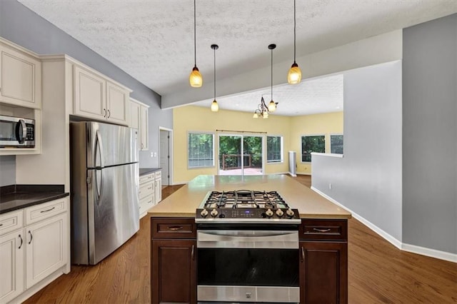kitchen with appliances with stainless steel finishes, dark wood-style floors, a textured ceiling, hanging light fixtures, and dark brown cabinets