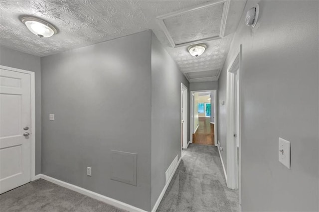 corridor with attic access, carpet, baseboards, and a textured ceiling