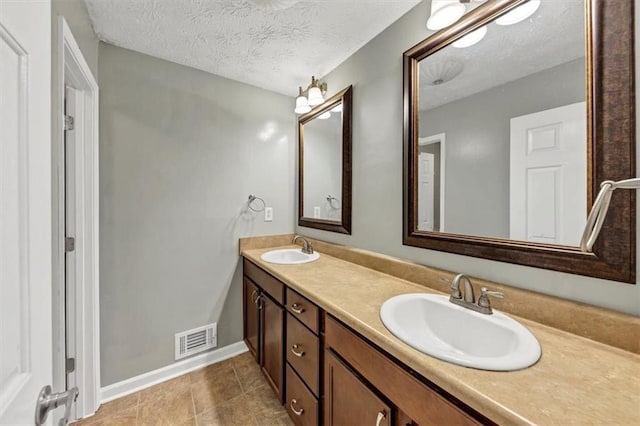 bathroom with double vanity, a textured ceiling, and baseboards