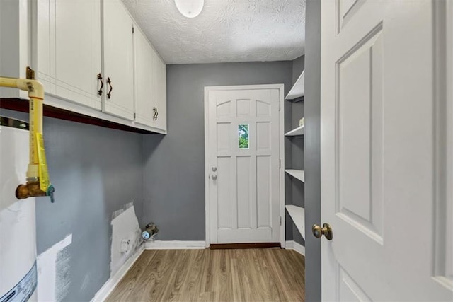 washroom featuring light wood finished floors, baseboards, cabinet space, a textured ceiling, and water heater