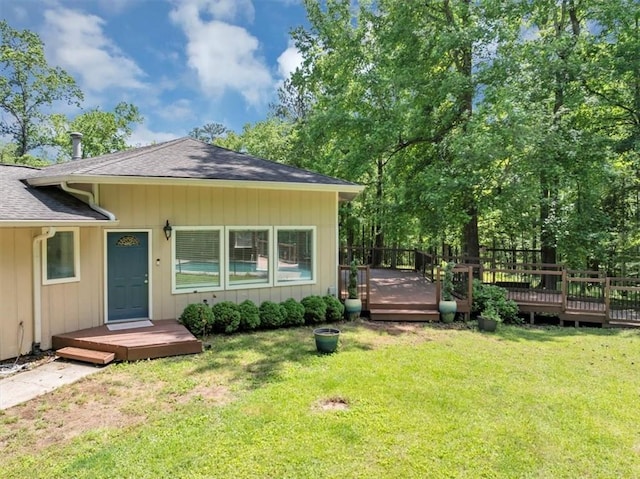 view of front facade with a deck, a front lawn, and a shingled roof