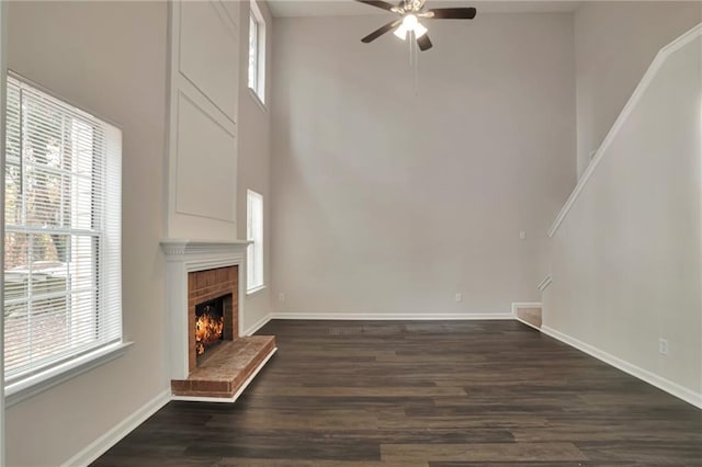 unfurnished living room featuring dark hardwood / wood-style flooring, a brick fireplace, plenty of natural light, and ceiling fan