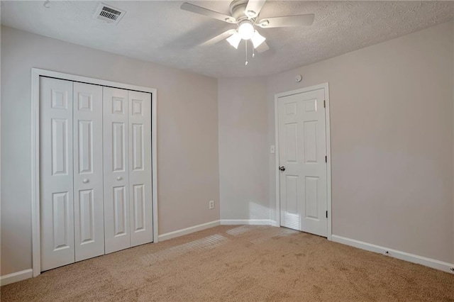 unfurnished bedroom featuring ceiling fan, light colored carpet, a textured ceiling, and a closet