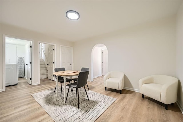 dining area featuring arched walkways, baseboards, washer / dryer, stairs, and light wood-style flooring