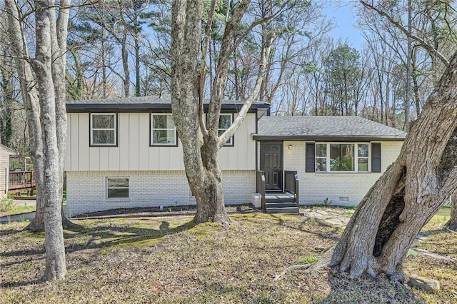 tri-level home featuring a shingled roof, board and batten siding, crawl space, and brick siding