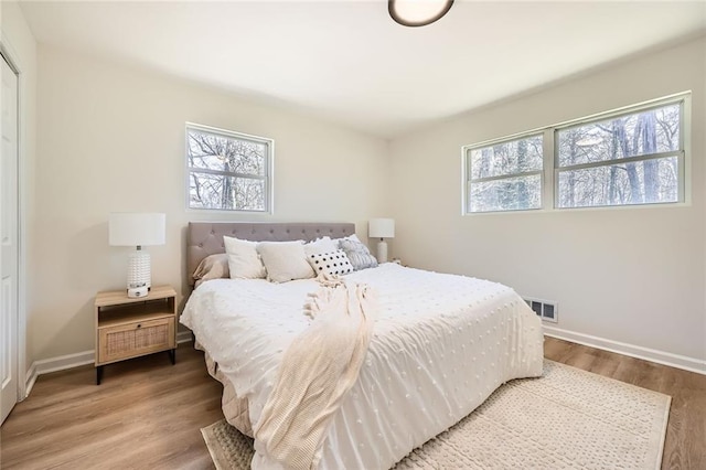 bedroom featuring baseboards, multiple windows, wood finished floors, and visible vents
