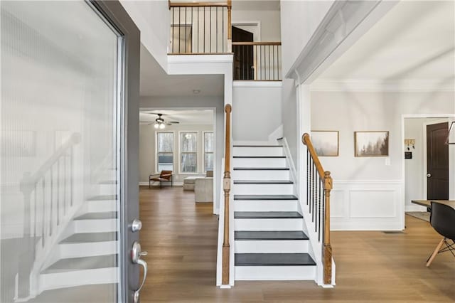 foyer entrance with stairs, crown molding, a decorative wall, and wood finished floors