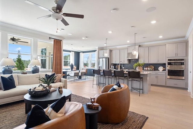 living room with light hardwood / wood-style floors, sink, crown molding, and ceiling fan