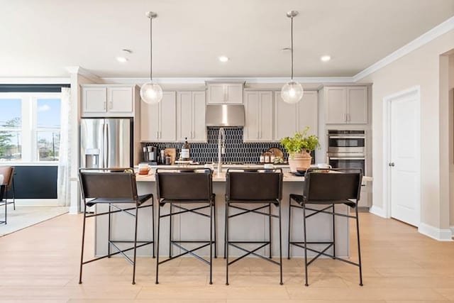 kitchen with pendant lighting, a center island with sink, a breakfast bar, appliances with stainless steel finishes, and ornamental molding