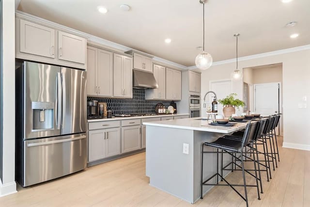 kitchen featuring appliances with stainless steel finishes, a kitchen bar, decorative light fixtures, gray cabinets, and a kitchen island with sink