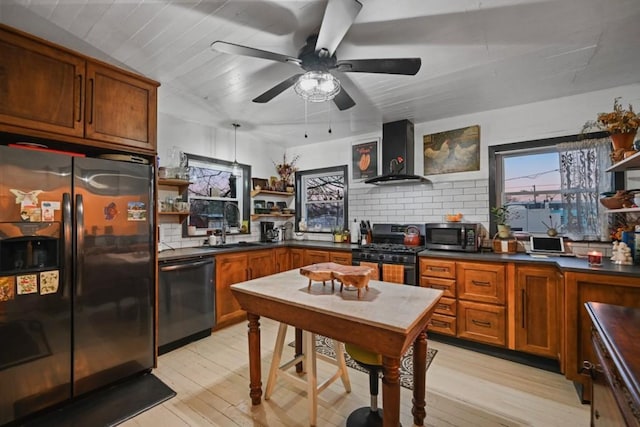 kitchen featuring decorative backsplash, light wood-type flooring, wall chimney exhaust hood, and appliances with stainless steel finishes