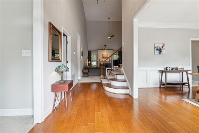 foyer with ornamental molding, hardwood / wood-style flooring, ceiling fan, and a high ceiling