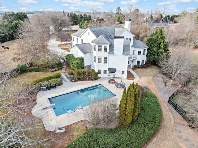 back of house featuring stairway, a chimney, fence, an outdoor pool, and a patio area