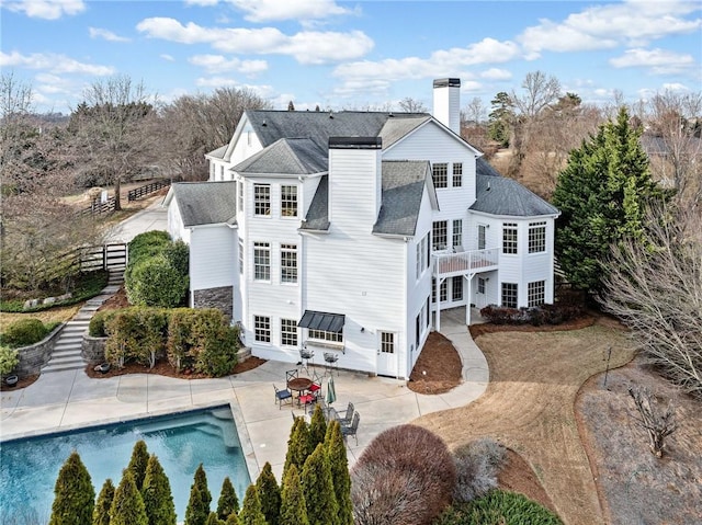 rear view of property featuring a chimney, an outdoor pool, a balcony, a patio, and roof with shingles