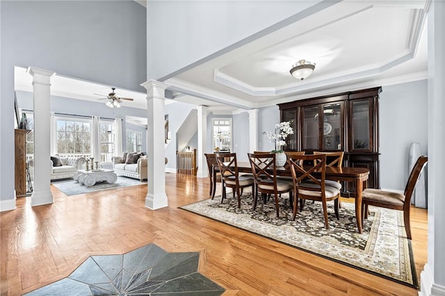 dining room featuring a raised ceiling, crown molding, wood finished floors, and decorative columns