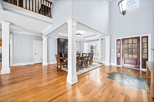 entrance foyer featuring a towering ceiling, ornate columns, ornamental molding, light wood-type flooring, and baseboards
