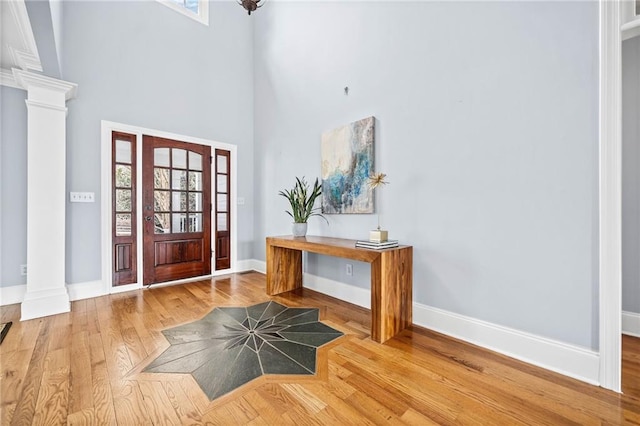 entrance foyer featuring baseboards, wood finished floors, a towering ceiling, and ornate columns