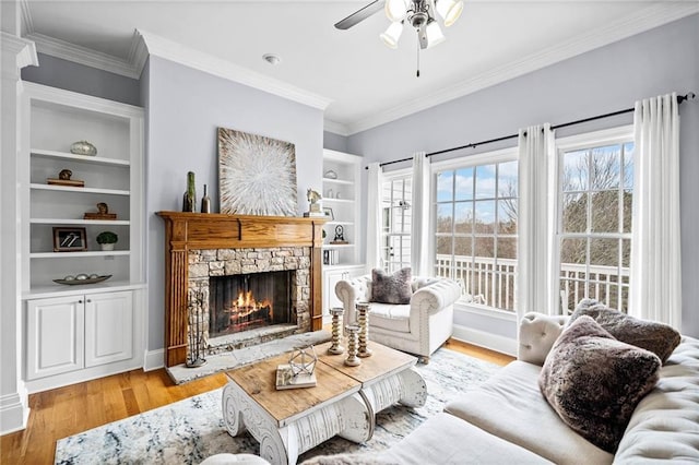living area featuring ornamental molding, a fireplace, a ceiling fan, and light wood-type flooring