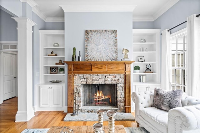 living area featuring wood finished floors, decorative columns, a stone fireplace, and ornamental molding