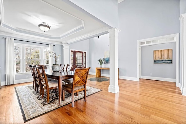 dining space with crown molding, a tray ceiling, light wood-type flooring, and decorative columns