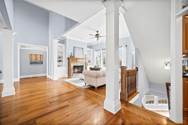 living room featuring light wood-type flooring, a lit fireplace, ceiling fan, and a healthy amount of sunlight
