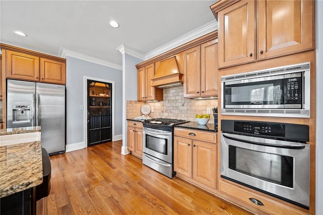 kitchen with light stone counters, crown molding, stainless steel appliances, premium range hood, and baseboards