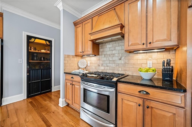 kitchen featuring dark stone counters, light wood-style floors, stainless steel range with gas stovetop, baseboards, and ornamental molding