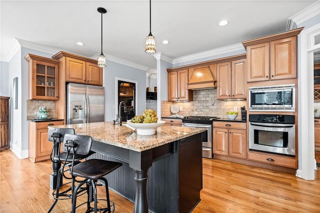 kitchen with light stone counters, ornamental molding, premium range hood, backsplash, and appliances with stainless steel finishes